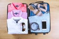 Open suitcase with trendy female clothes and accessories on wooden floor top view, copy space, vintage toned image. Packing luggag Royalty Free Stock Photo