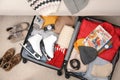 Open suitcase with warm clothes, accessories and shoes near sofa indoors, flat lay