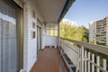 Open terrace of a house in a residential building with white painted railings, brown floors and views of a community garden with