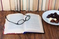 Open textbook, glasses and chocolate candies on white plate, stack of old book on wooden table, education concept background, many