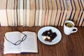 Open textbook, glasses, cup of tea and chocolate candies on white plate, stack of old book on wooden table, education concept