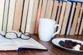Open textbook, glasses, cup of tea and chocolate candies on white plate, stack of old book on wooden table, education concept Royalty Free Stock Photo