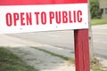 open to public sign on wood wooden post with road and sidewalk behind, close up. p