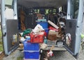 Open, untidy trunk of a delivery van, loaded with old tools, scrap and garbage
