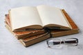 An open vintage book or notebook in a dust jacket on a stack of old shabby books and reading glasses Royalty Free Stock Photo