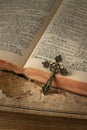 Open vintage holy bible with german text in old print and metal catholic cross with crucifix and ornament on torn paper background