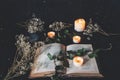 Open vintage poetry book on black table surface with white lit burning candles and dried flowers