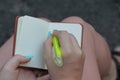 Open white notebook and a green pen in the hands of a girl over her feet on the street