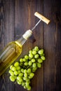 Open the wine concept. Corkscrew into cork of white wine bottle near bunch of grapes on dark wooden background top view Royalty Free Stock Photo