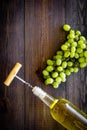 Open the wine concept. Corkscrew into cork of white wine bottle near bunch of grapes on dark wooden background top view Royalty Free Stock Photo