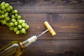 Open the wine concept. Corkscrew into cork of white wine bottle near bunch of grapes on dark wooden background top view Royalty Free Stock Photo