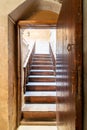 Open wooden door revealing wooden old staircase going up with with reflections of the stairs on the door