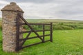 Open wooden gate into farmers green field. Old stone pillar.