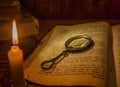 An open ancient prayer book and a magnifying glass on its open pages under the light of a candle