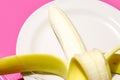 Opened banana on dish on pink background with copy space