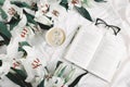 Opened book, coffee cup, glasses, fresh flowers on the white bed. Flat lay, top view Royalty Free Stock Photo