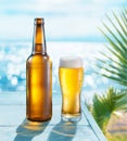 Opened bottle of beer and beer glass with condensation on the wooden table. Blurred sparkling sea at the background. Summer vibes