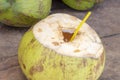 Opened coconut with straw ready for drinking. Fresh coco water photo. Coconut fruit on wooden table.