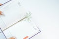 Opened diary with green small flowers between pages lying on white table. Woman holding sketchpad with empty notes. Royalty Free Stock Photo