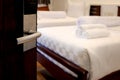 Opened door with blurred background of stack of fresh white bath towels on white bed in hotel room, travel and convenient