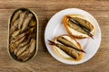 Opened jar with sprats, sandwiches with mayonnaise and sprats in plate on wooden table. Top view