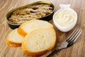 Opened jar with sprats, slices of bread, bowl with mayonnaise, fork on wooden table