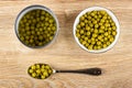 Opened jar, white bowl with canned green peas, spoon with green peas on wooden table. Top view