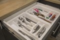 Opened kitchen drawer with a tray and cutlery inside. Grey front of the drawer, white inside, handless design