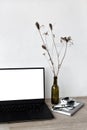 Opened laptop with blank white scree standing on beige wooden desk, stationary, vase with flowers, minimalist home Royalty Free Stock Photo