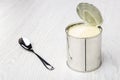 Opened metallic jar with sweet condensed milk, spoon on table Royalty Free Stock Photo