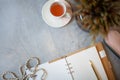 Opened notebook with clean sheets, gold pen, rosary, pink colored case and cup of tea near vase