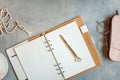 Opened notebook with clean sheets, gold pen, rosary, pink colored case and cup of tea near vase