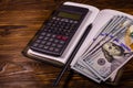 Opened notepad, one hundred dollar banknotes, scientific calculator and pencil on wooden table Royalty Free Stock Photo