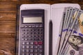 Opened notepad, one hundred dollar banknotes, scientific calculator and pencil on wooden table. Top view Royalty Free Stock Photo