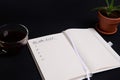 Opened notepad, organizer with list to do on blank white sheets, cup of coffee and potted succulent in clay pot, on black