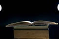 Opened old book on stack of books, dark background ,visible lights Royalty Free Stock Photo