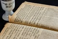 An opened old Jewish Bible and white porcelain kiddush wine cup on black background. Selective focus Royalty Free Stock Photo