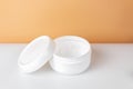 Opened plastic container jar with cream on a white table and orange background Royalty Free Stock Photo