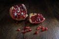 Opened pomegranate fruit with red juicy seeds on rustic wood, dark and moody style, copy space