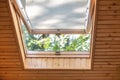 Opened roof window with blinds or curtain in wooden house attic. Room with slanted ceiling made of natural eco materials