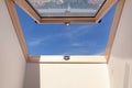 Opened roof window dormer with white wall against blue sky.