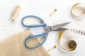 Opened scissors, tailor`s tape measure, threads and pins on a white background.