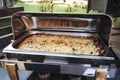 Opened stainless hotel pans on food warmer with baked meal. Self-service buffet table. Celebration, party, birthday or