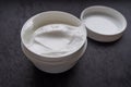 Opened white jar of cosmetic face cream with lid on a black slate background Royalty Free Stock Photo