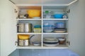 Opened white kitchen cupboard with plates, metal pots and food containers Royalty Free Stock Photo