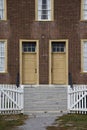 Opened white picket fence gate leads to two yellow antique doors. Royalty Free Stock Photo