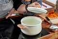 Opened white saucepan with wood pens on the black stove. Cooking a soup - water boiling, check and preparation. Woman`s hand