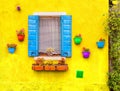 Opened window with blue shutters on a yellow wall. With red, green, orange,  blue, and purple flower pots. Royalty Free Stock Photo