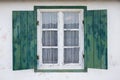 Opened wooden window with green shutters, white facade