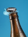 Opening beer bottle on blue background. Gas cloud going out of the beer bottle blowing the cap Royalty Free Stock Photo